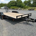 a flatbed trailer is parked in a gravel lot .