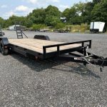 a carry on flatbed trailer is parked in a gravel lot .