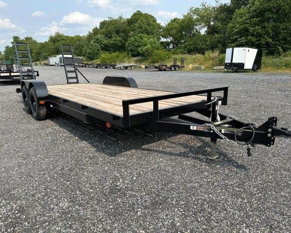 a carry on flatbed trailer is parked in a gravel lot .