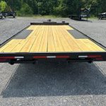 a flatbed trailer with a wooden deck is parked in a gravel lot .
