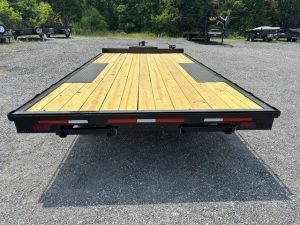 a flatbed trailer with a wooden deck is parked in a gravel lot .