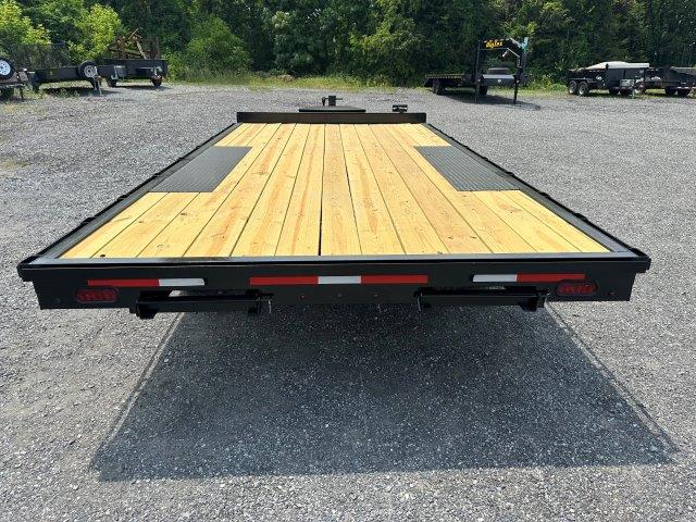 a flatbed trailer with a wooden deck is parked in a gravel lot .