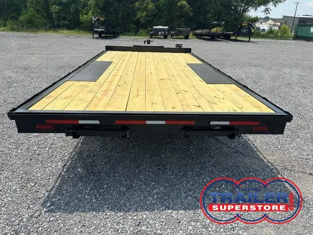 a trailer with a wooden deck is parked in a gravel lot .