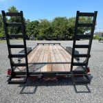 a trailer with a wooden deck and ladder on the back is parked in a gravel lot .