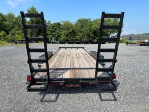 a trailer with a wooden deck and ladder on the back is parked in a gravel lot .