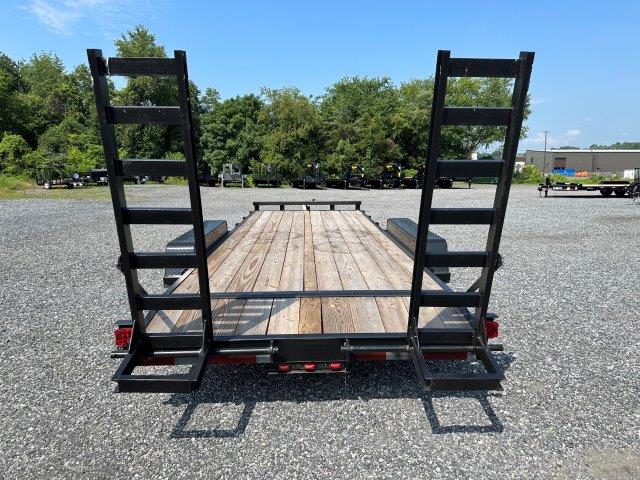 a trailer with a wooden deck and ladder on the back is parked in a gravel lot .