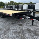 a flatbed trailer is parked in a gravel lot next to a row of trailers .