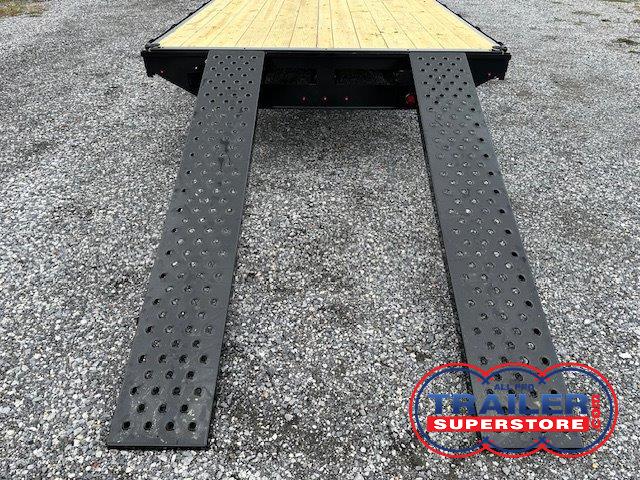 a trailer with ramps attached to it is sitting on top of a gravel road .