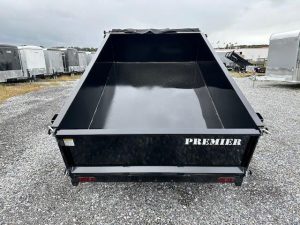 a black Premier dump trailer parked in a gravel lot