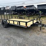 a trailer with a wooden deck is parked in a gravel lot .