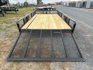 a trailer with a wooden deck and a metal ramp is parked on the side of the road .
