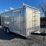 a trailer with a ladder on the back of it is parked in a gravel lot