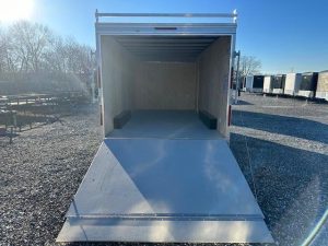 a white trailer is parked in a gravel lot with the door open .
