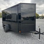 a black trailer is parked in a gravel lot .