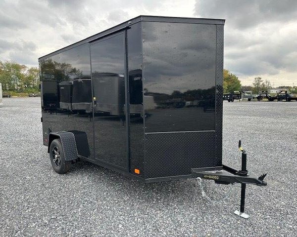a black trailer is parked in a gravel lot .