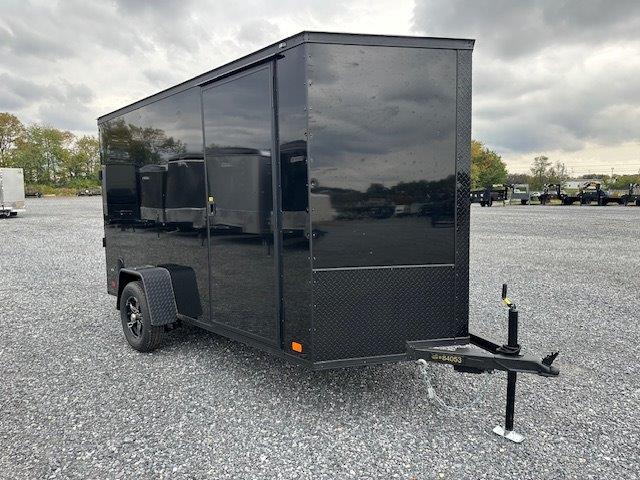 a black trailer is parked in a gravel lot .