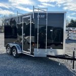 a black trailer with a ladder parked in a gravel lot