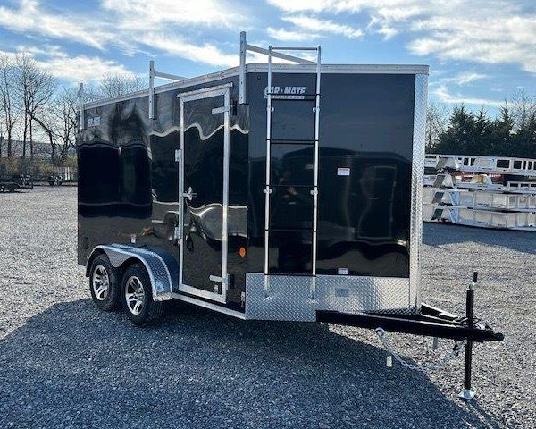 a black trailer with a ladder parked in a gravel lot