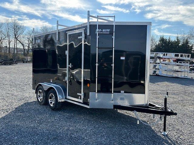 a black trailer with a ladder parked in a gravel lot