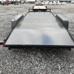 a black flatbed trailer is parked in a gravel lot .