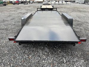 a black flatbed trailer is parked in a gravel lot .