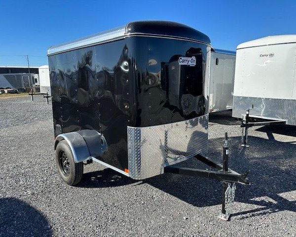 a black and silver trailer is parked in a gravel lot .