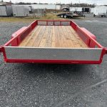 a red trailer with a wooden floor is parked in a gravel lot .