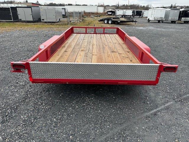 a red trailer with a wooden floor is parked in a gravel lot .