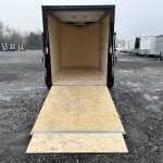 an atc trailer with the door open is parked in a gravel lot .