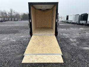 an atc trailer with the door open is parked in a gravel lot .