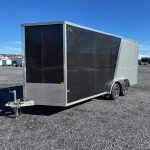 a black and silver trailer is parked in a gravel lot