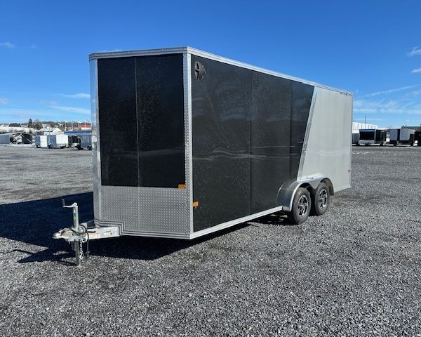 a black and silver trailer is parked in a gravel lot