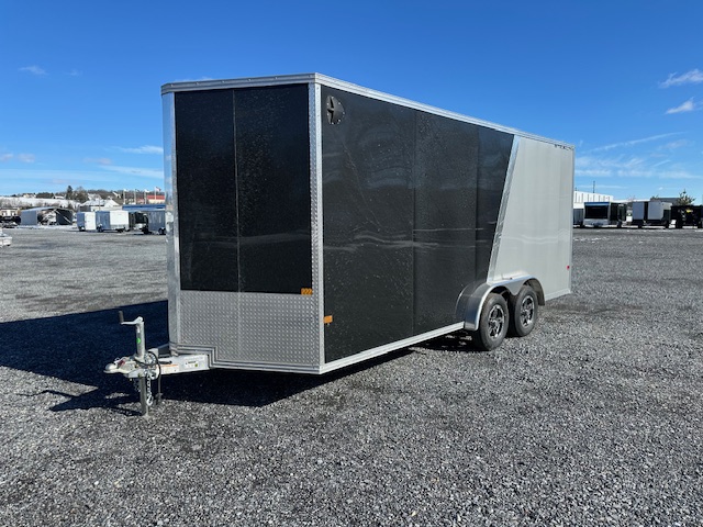 a black and silver trailer is parked in a gravel lot