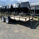 a Car Mate trailer with a wooden deck parked next to a row of dump trailers
