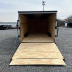 a trailer with a wooden floor is sitting in a gravel lot .