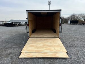 a trailer with a wooden floor is sitting in a gravel lot .