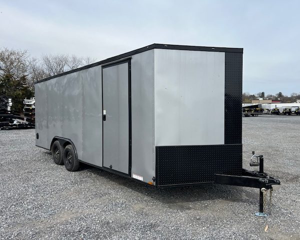 a gray and black trailer is parked in a gravel lot