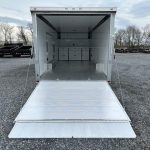 a white trailer with the door open is parked in a gravel lot .