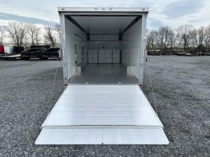 a white trailer with the door open is parked in a gravel lot .