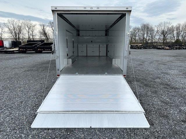 a white trailer with the door open is parked in a gravel lot .