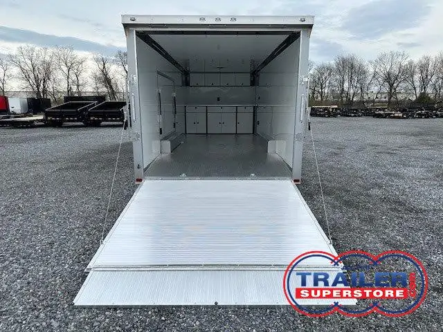 a white trailer with the door open is parked in a gravel lot .