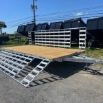 an Alcom trailer with a wooden deck parked next to a row of dump trailers