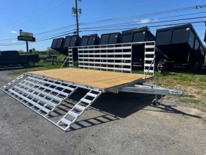an Alcom trailer with a wooden deck parked next to a row of dump trailers