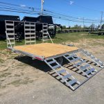an Alcom trailer parked next to dump trailers