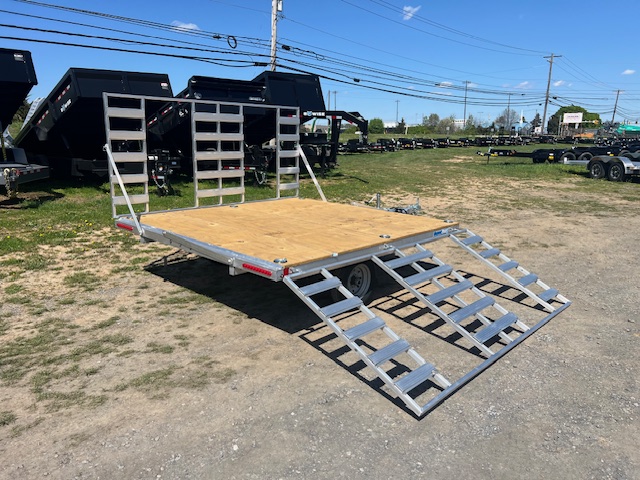 an Alcom trailer parked next to dump trailers