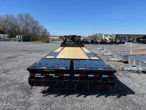 a flatbed trailer is parked in a gravel lot .