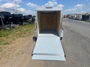 a white trailer with a ramp is parked on the side of the road .