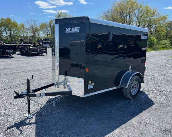 a black car-mate trailer is parked in a gravel lot