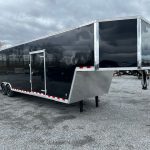 a black trailer is parked in a gravel lot .