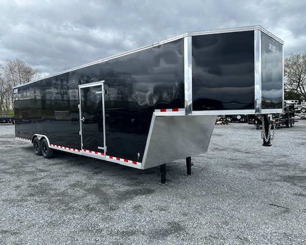 a black trailer is parked in a gravel lot .